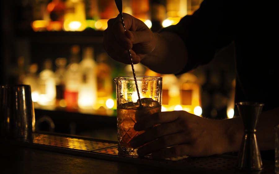 A bartender stirring a drink in front of backlit bottles